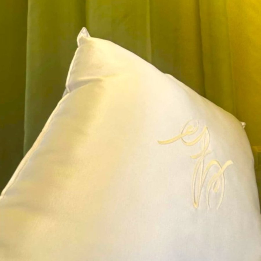 segno gg cuscino bianco e tenda in velluto verde gani the sign quadrata Cuscino bianco con il segno GG davanti a una tenda in velluto verde